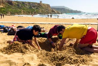 Líder do grupo e crianças cavando um buraco na praia